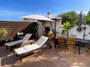 A patio with two lounge chairs, a table, and chairs, surrounded by potted plants and a pergola. - Matias Terrace House (Lourinhã)