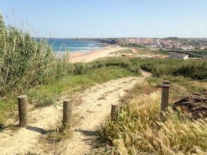 A coastal path leading to a beach with a view of a town in the distance. - Casa Matias - Charming Portuguese Beach House (Lourinhã)