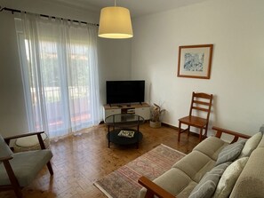 A living room with a television, a wooden chair, a sofa, a coffee table, and a painting on the wall. - Matias Terrace House (Lourinhã)