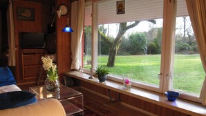 A cozy living room with a wooden interior, a television, a clock, and a window with a view of a green lawn. - Pleasant, modern and cozy, our apiary (Ulsnis)