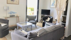 Ein modernes Wohnzimmer mit einem grauen Sofa, einem Glastisch, einem Fernseher und einem Kamin.