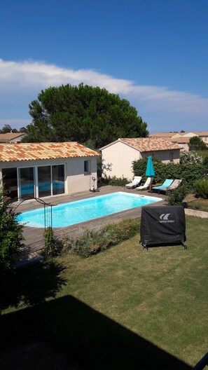 Una piscina con cubierta de madera, un patio techado y vistas a casas vecinas.