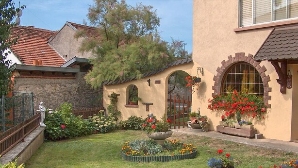 A courtyard with a garden, a stone wall, and a building with a tiled roof.
