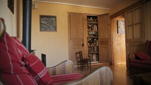 Ein gemütliches Wohnzimmer mit Holztür zu einem Stauraum, einem Kamin und einem roten, gemusterten Sofa.