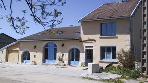 Ein zweistöckiges Gebäude mit einem Ziegeldach, einem Hauseingang mit einer blauen Tür und einem kleinen Garten mit Gartenmöbeln.