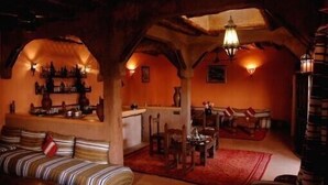 A cozy, rustic interior with a wooden ceiling, a seating area with striped cushions, and a dining table with chairs. - Riad of charm any comfort with swimming pool without opposite and big sported garden. (Marrakech)