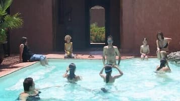 Une zone autour d’une piscine, avec des personnes dans l’eau et d’autres assises au bord.