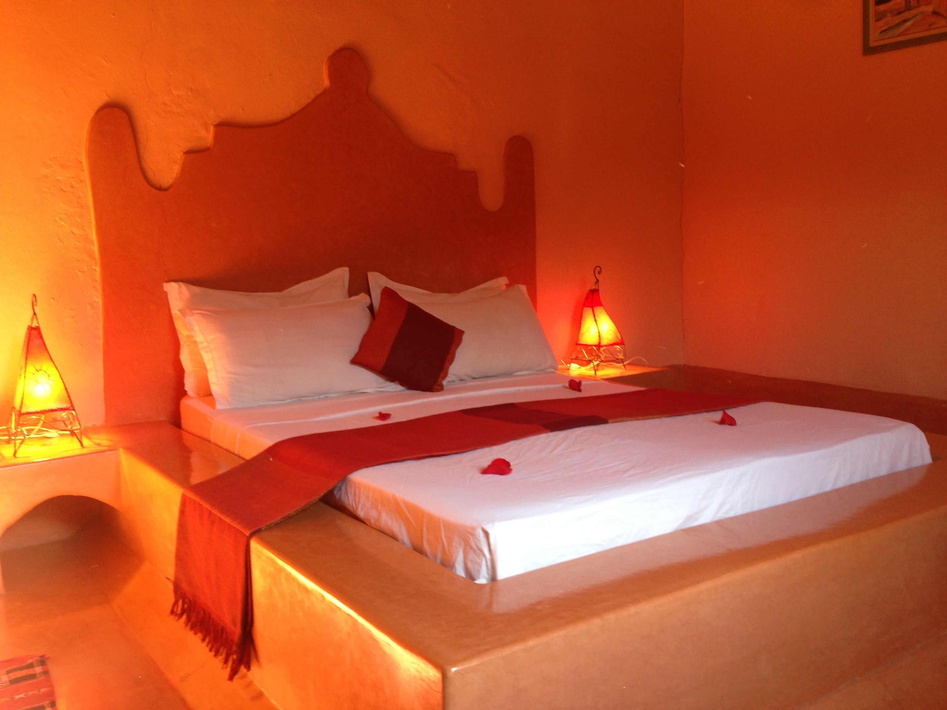 A bed with white linens, a red throw blanket, and two bedside lamps.