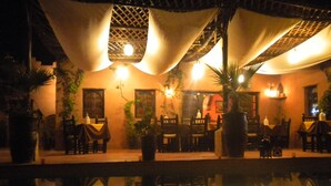 An outdoor dining area with tables and chairs, a pool reflecting the surroundings, and a building with a warm-toned facade. - Riad of charm any comfort with swimming pool without opposite and big sported garden. (Marrakech)