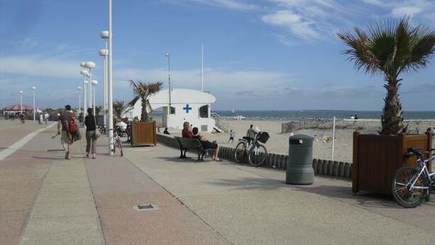 A coastal walkway with benches, a lifeguard station, and a beach in the background.