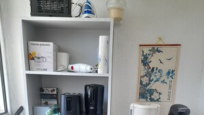 A kitchen with a microwave, toaster, coffee maker, and a small oven on a white shelf.