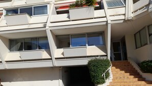 A multi-story building with a parking area, a staircase, and a small green plant on the ground floor.