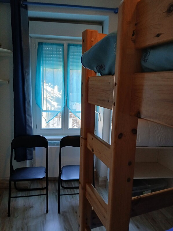 A room with a bunk bed, two chairs, and a window with blue curtains.