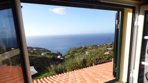 A window with a view of a coastal landscape, including terraced roofs and greenery. - sea view everywhere in the house (Estreito da Calheta)
