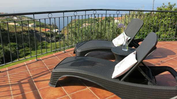 A balcony with two wicker lounge chairs, one with a cushion and a vase of flowers. - sea view everywhere in the house (Estreito da Calheta)