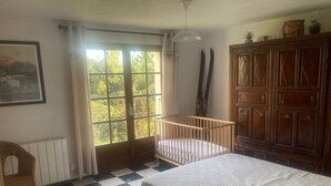 Una habitación con suelo a cuadros, una cuna, un armario de madera y un ventanal con cortinas.
