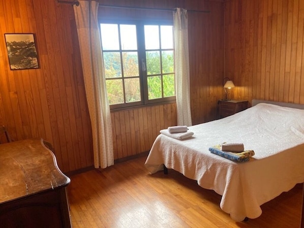 A room with a bed, a chair, a window with curtains, and a picture on the wall.