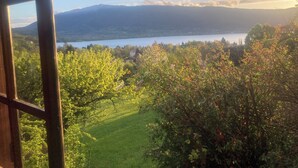 Vista desde una ventana sobre un lago, montañas y un área con césped y árboles.