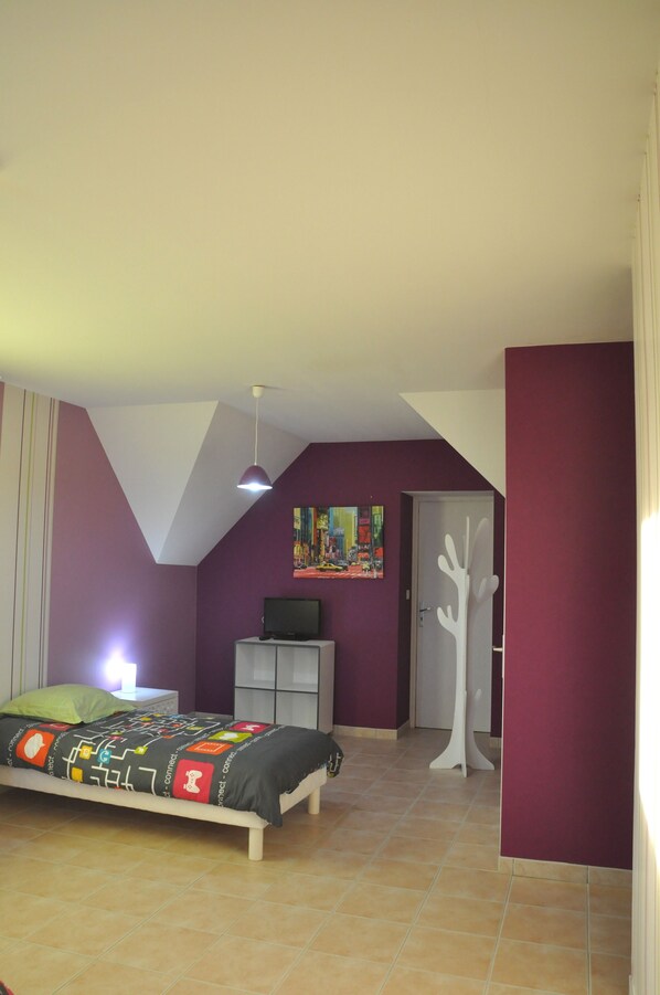 A bedroom with a bed, a nightstand, a television, a door, and a wall painting. - Crucano palm groves, the house itself has a heated swimming pool for 10 people (Plouharnel)