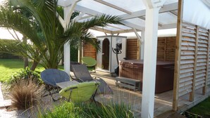 An outdoor patio with a wooden deck, a covered seating area, a hot tub, and a wooden cabin structure in the background. - Crucano palm groves, the house itself has a heated swimming pool for 10 people (Plouharnel)