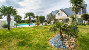 A house with a swimming pool, surrounded by a well-maintained lawn and palm trees. - Crucano palm groves, the house itself has a heated swimming pool for 10 people (Plouharnel)
