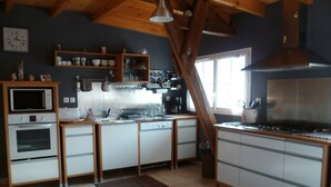 A kitchen with white cabinets, a microwave, oven, and a stove. There are shelves with dishes and a clock on the wall.