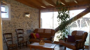 A cozy living room with stone walls, wooden furniture, a large window, and a potted plant.