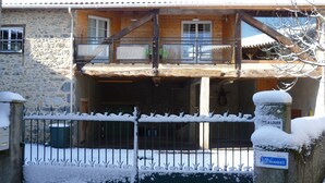 A two-story stone house with a wooden balcony and a metal gate covered in snow.
