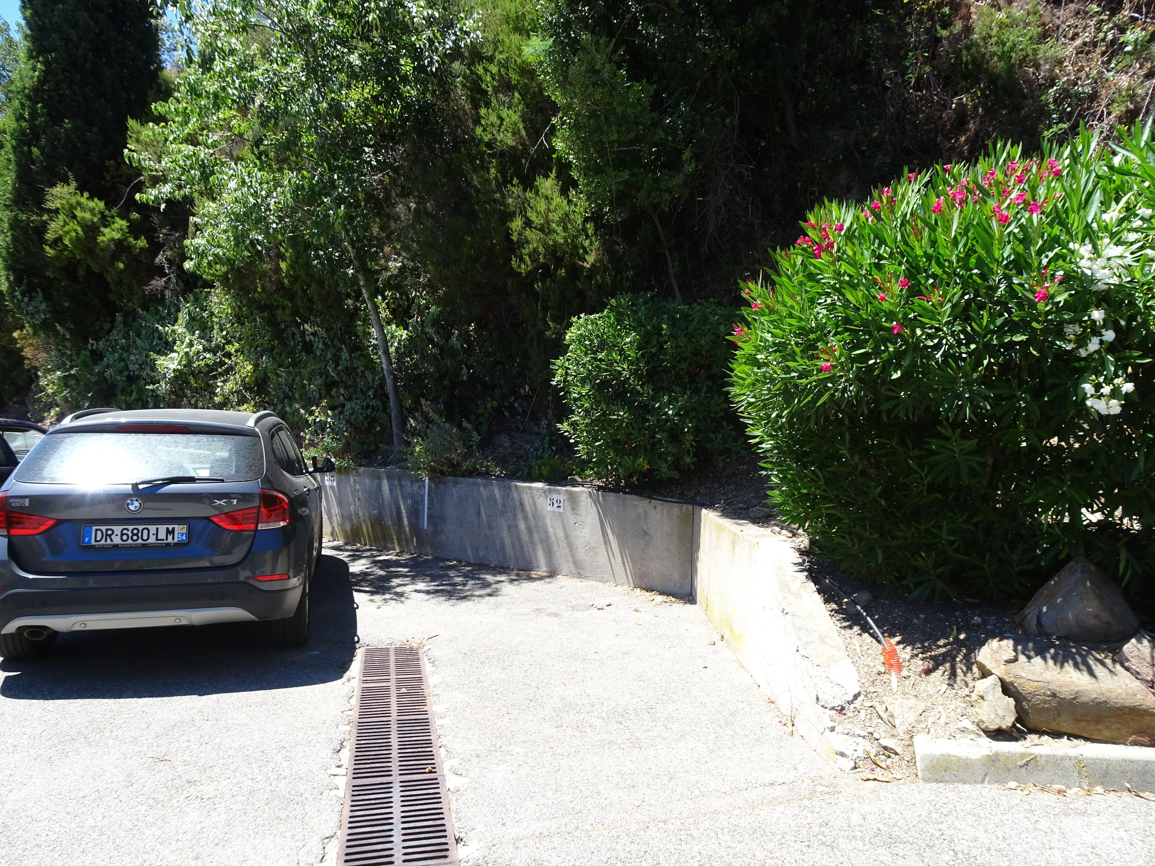 Une aire de stationnement où est garée une BMW X7, entourée de verdure et délimitée par une barrière en béton.