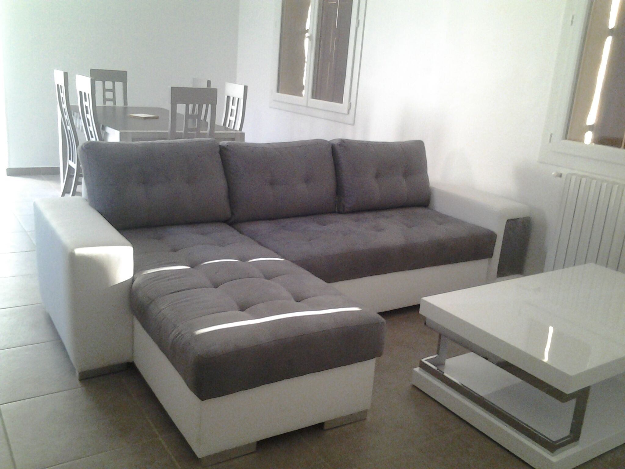 Un salon moderne avec un canapé d’angle gris, un pouf blanc et une table basse blanche.