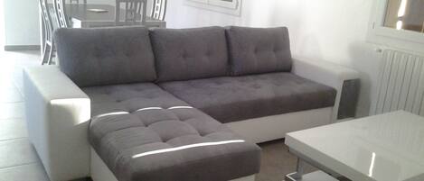 A modern living room with a grey sectional sofa, a white ottoman, and a white coffee table.