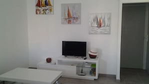 Una sala de estar con un televisor de pantalla plana sobre un mueble blanco, una mesa de centro blanca, un sofá gris y tres cuadros en la pared.