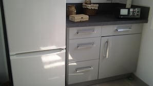 Una cocina con refrigerador, microondas y un mueble pequeño con cajones.