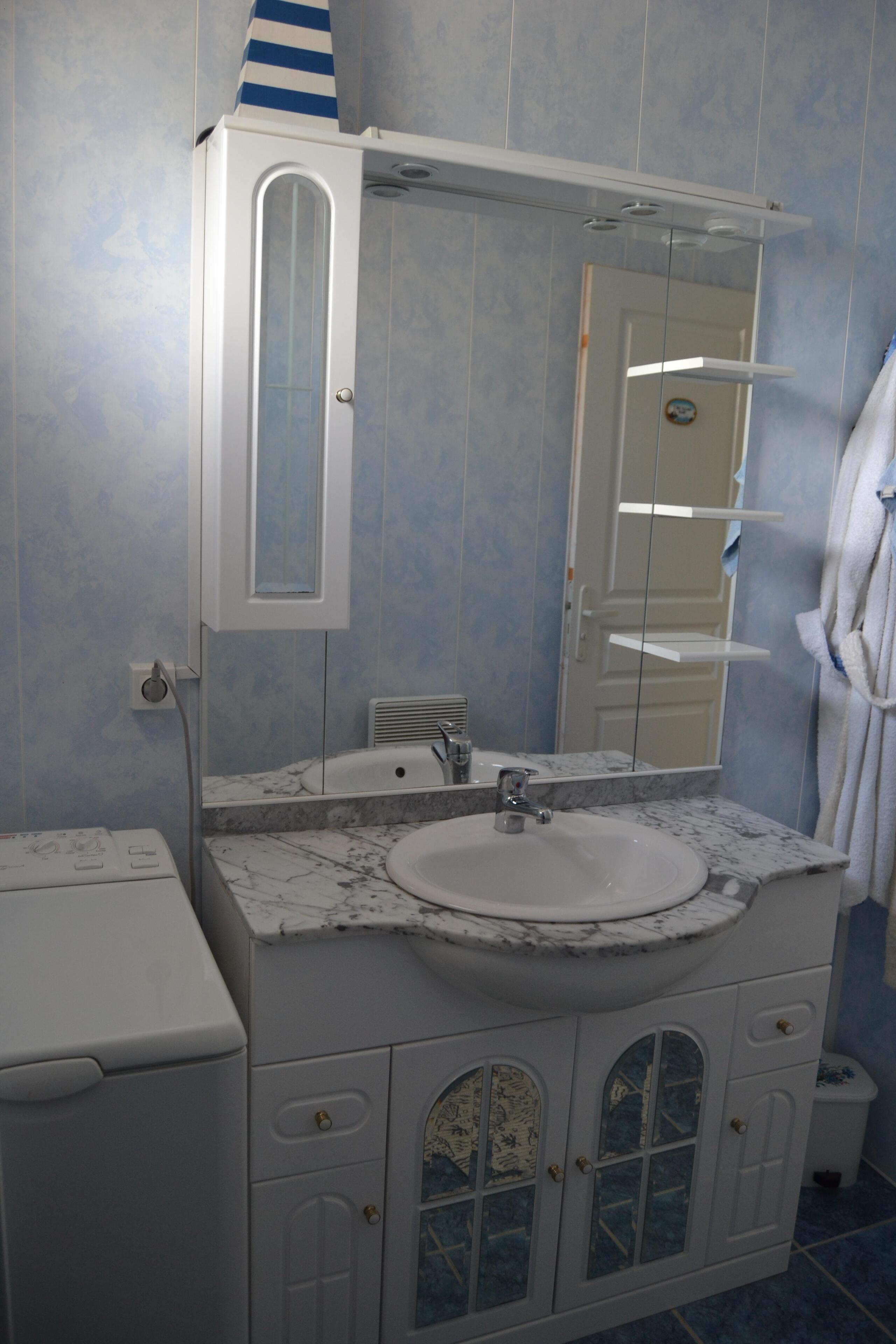 Un baño con lavamanos blanco, espejo y armario.