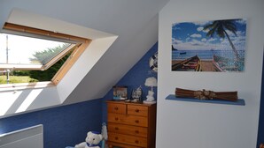 Ett barnrum med ett sluttande tak, en byrå i trä, ett litet bord och en väggdekoration med strandtema.