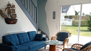 Ett vardagsrum med en blå soffa, ett tillhörande soffbord, flätade stolar, ett runt bord och en trappa med blå väggar.