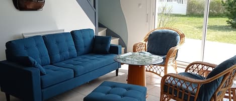 Ett vardagsrum med en blå soffa, ett tillhörande soffbord, flätade stolar, ett runt bord och en trappa med blå väggar.