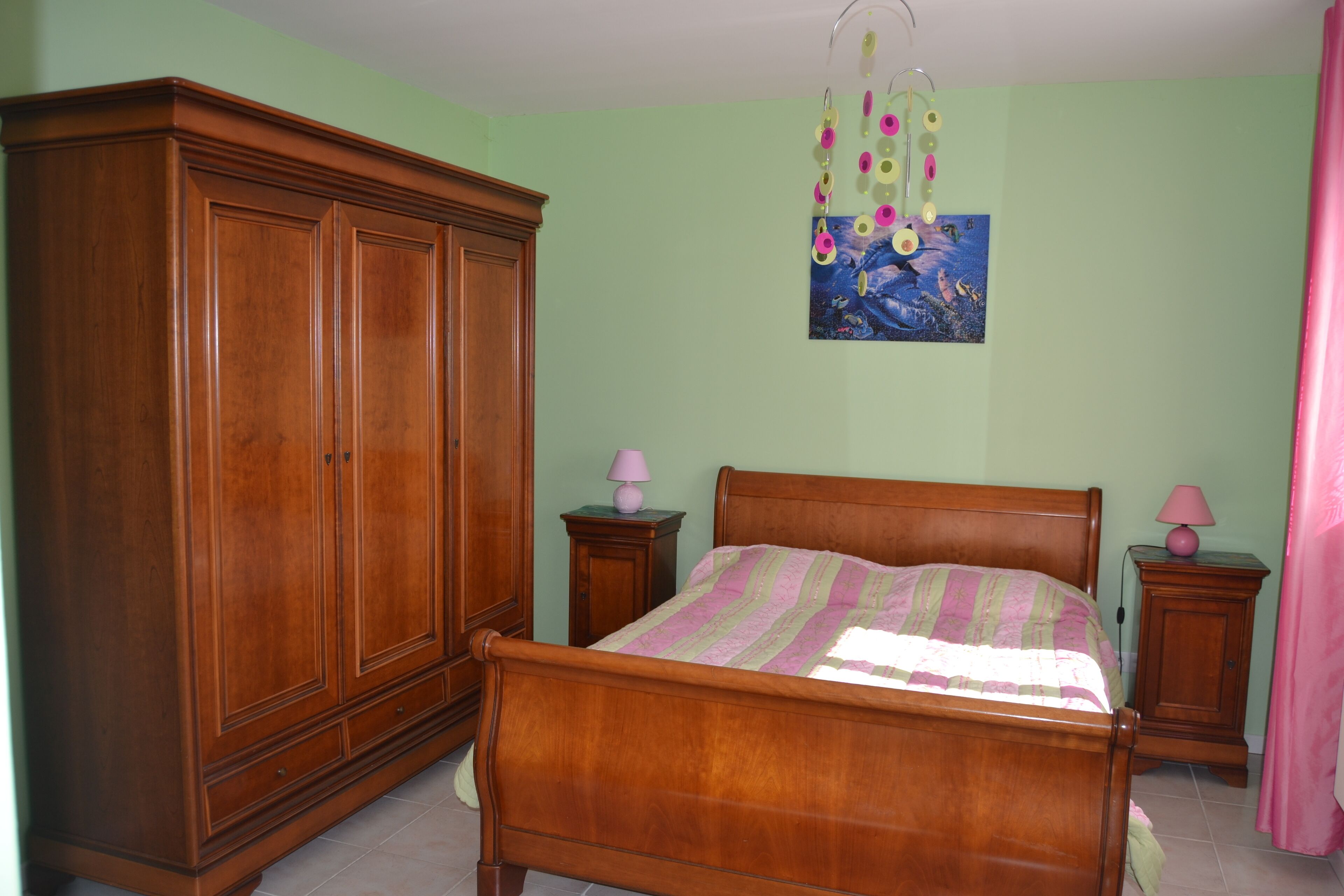A bedroom with a wooden bed, two bedside tables with lamps, a wardrobe, and a wall hanging.
