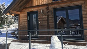 Een houten blokhut met een zwarte deur en grote ramen, omringd door sneeuw.