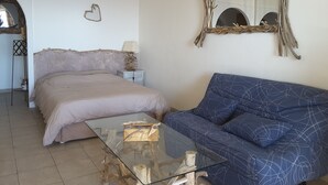 A bedroom with a bed, a glass coffee table, a blue sofa, a mirror with a branch frame, and a wall-mounted heart decoration.