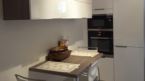 A modern kitchen with white cabinets, a microwave, and a refrigerator. There is a dining table with chairs and a basket of bread.