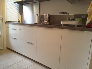 Una cocina con armarios blancos, un lavamanos de acero inoxidable y una ventana con persianas.