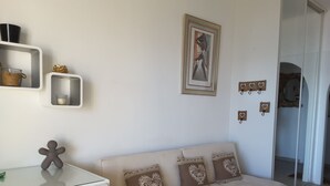 A modern living room with a white sofa, a glass-top desk, and a framed picture on the wall.