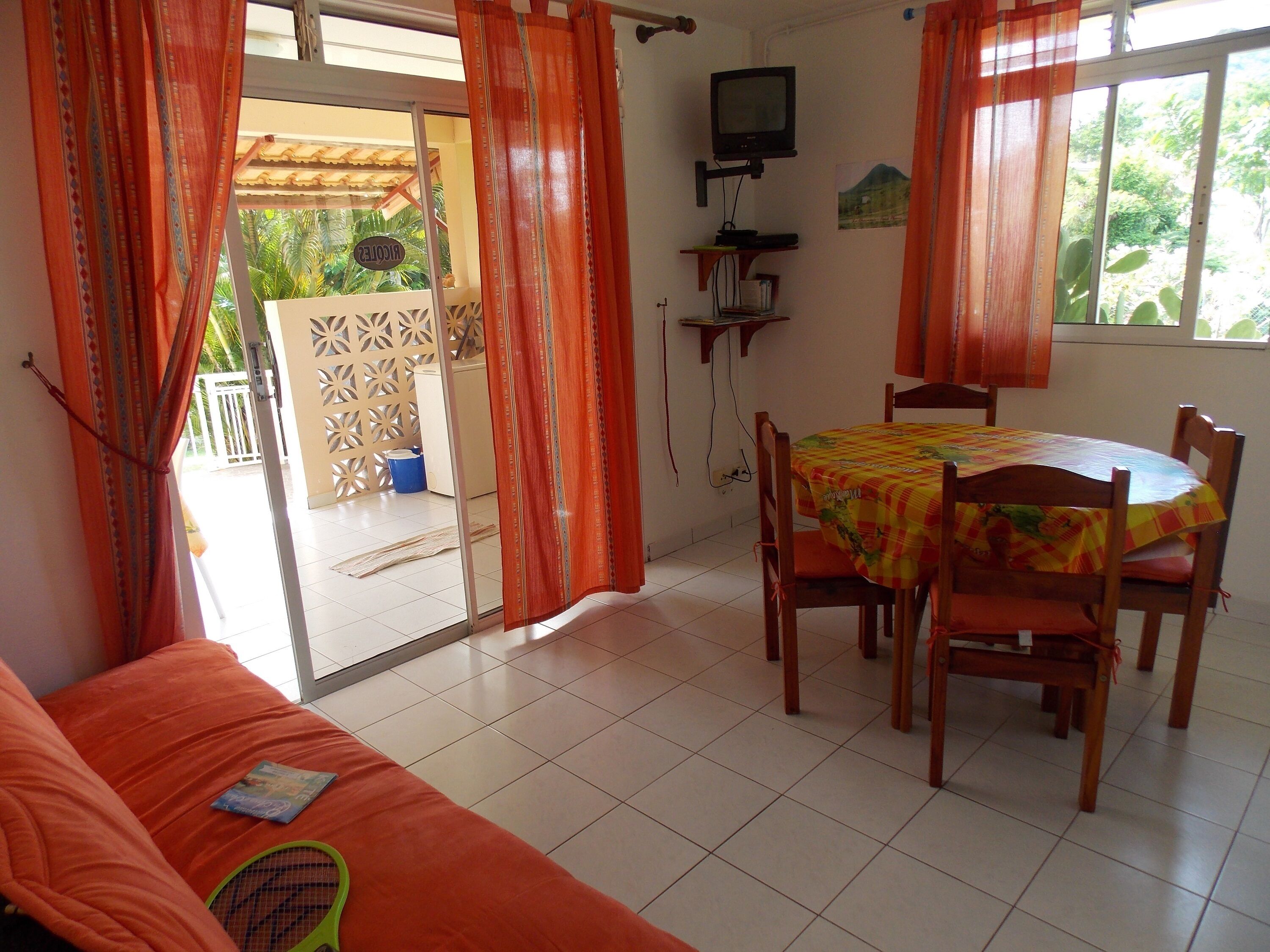 A room with a sofa, a dining table with chairs, a television on a stand, and a window with curtains.