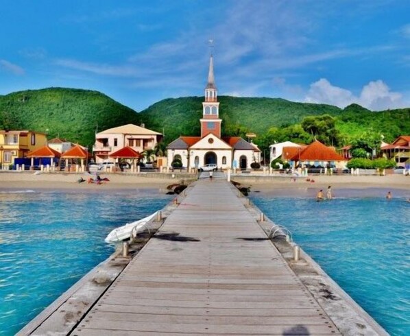 A wooden pier leading to a beach with a church in the background and mountains.
