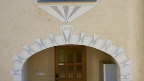 Entrada d'un edifici amb una porta de fusta, un petit finestral a dalt i un arc decoratiu.