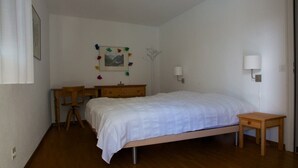 Habitació amb un llit individual, una petita còmoda de fusta, un escriptori i dues làmpades penjades a la paret.