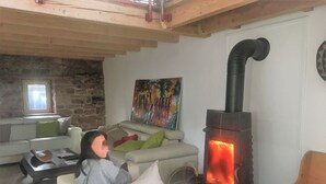 A cozy living room with a stone wall, a sofa, a coffee table, and a wood-burning stove. - Quiet house, with open view and all the comfort in the heart of Alsace (Saint-Pierre-Bois)