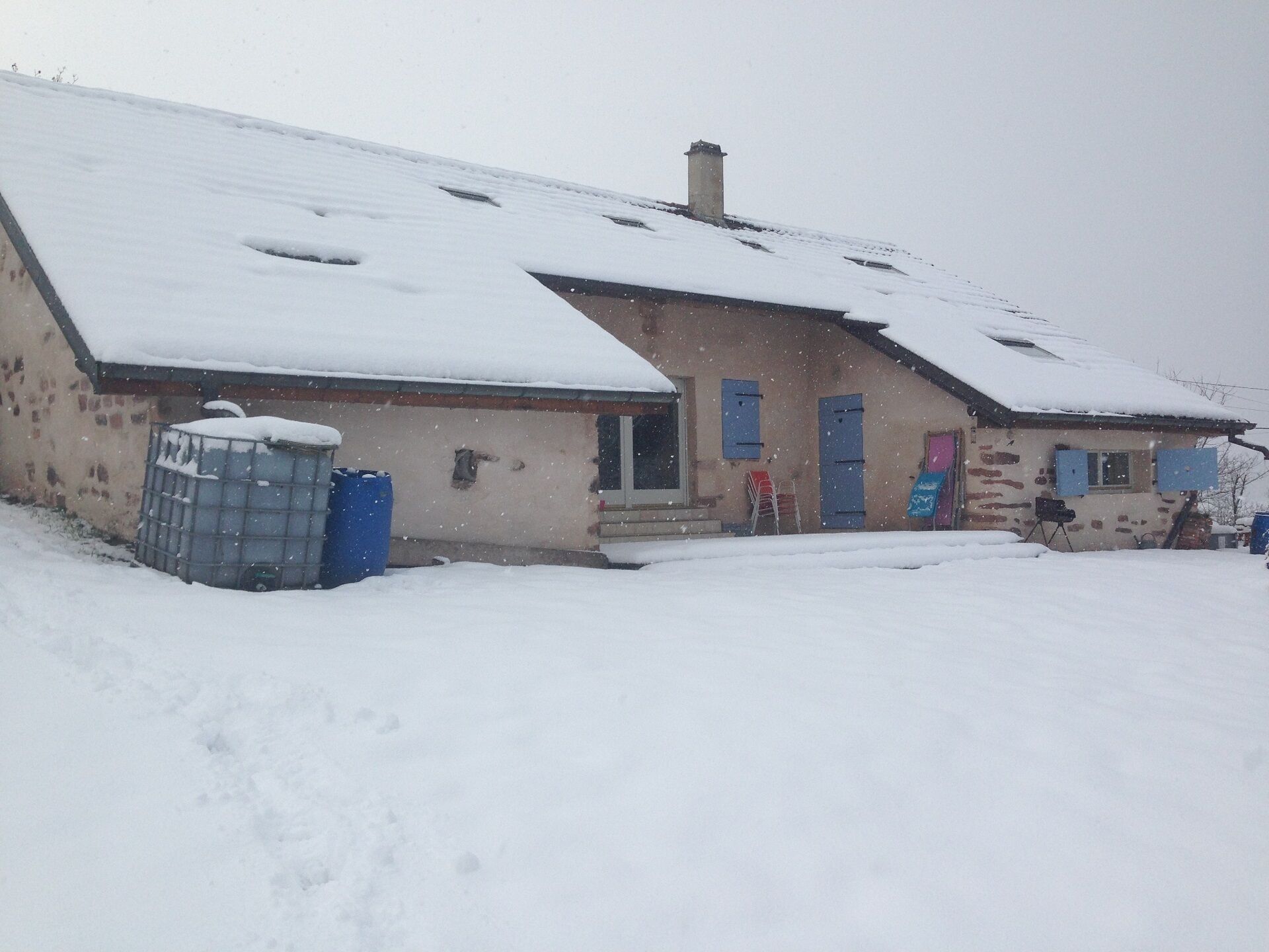 A building with a sloped roof covered in snow, a visible chimney, and a blue door.