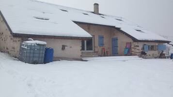 A building with a sloped roof covered in snow, a visible chimney, and a blue door.